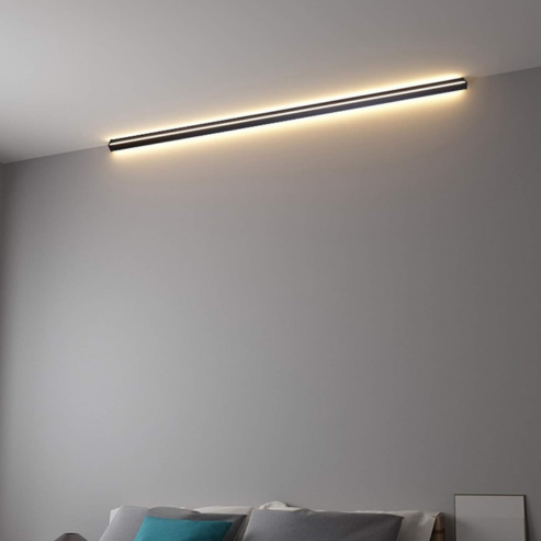 Applique LED linéaire noire installée horizontalement au-dessus d’un lit.
