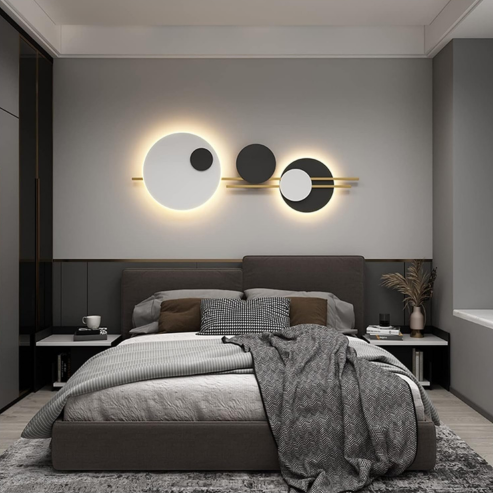 Applique à disques noirs et blancs avec barres dorées, au-dessus d’un lit.