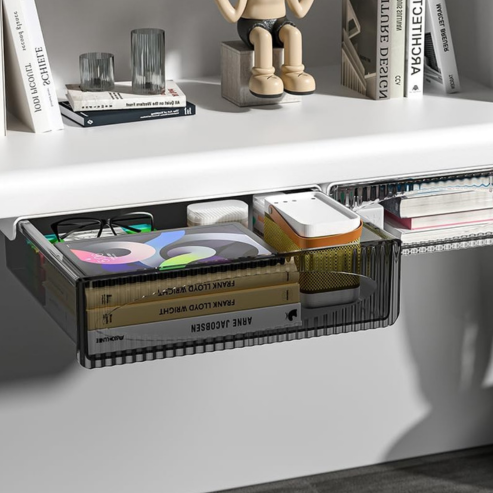 Tiroir transparent ouvert sous un bureau, contenant livres et petits objets.