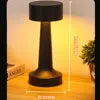 Lampe de table noire allumée, projetant une lumière chaude.