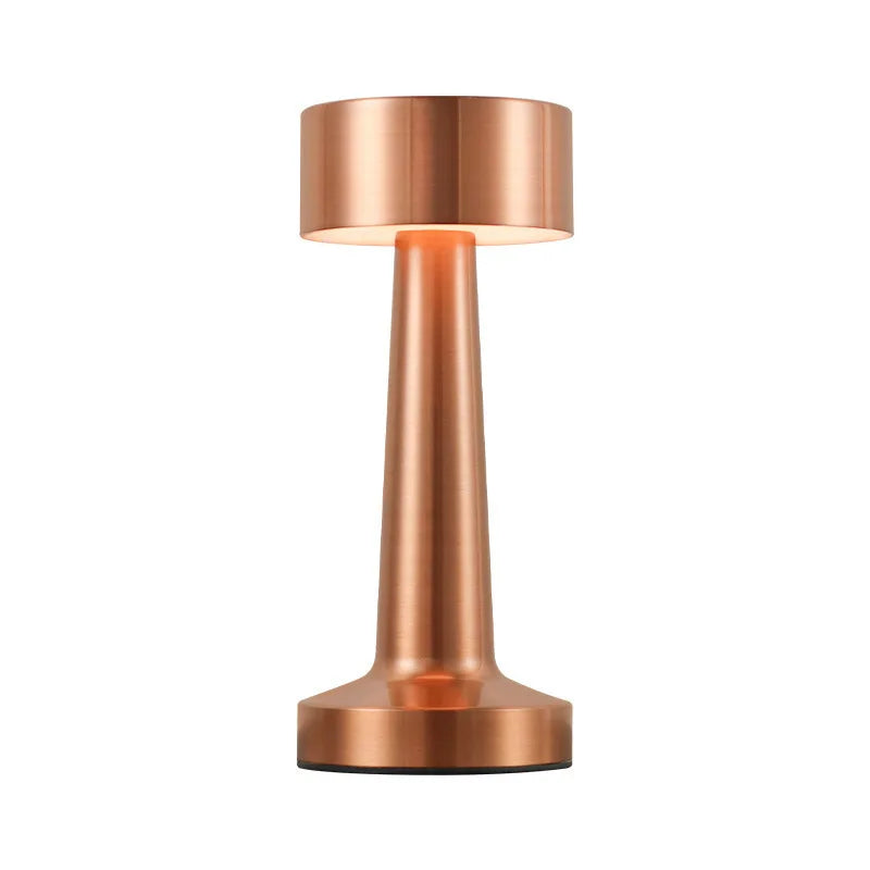 Lampe de table cuivrée allumée, présentée sur fond blanc.